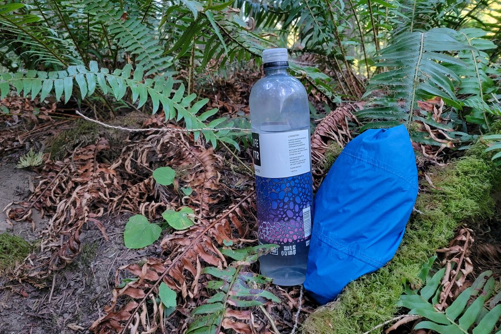 The Zpacks Vertice Jacket rolled up into a small ball sitting next to a water bottle